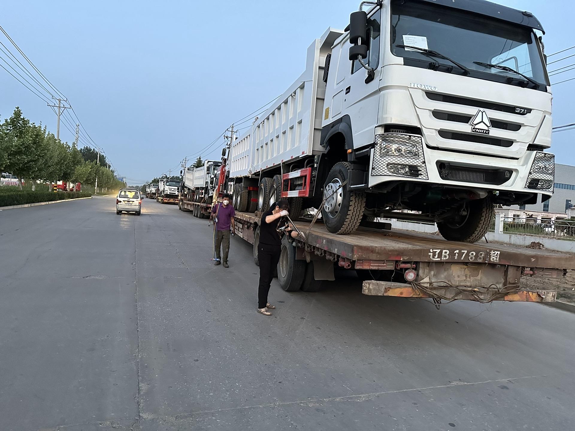 HOWO dump trucks being loaded onto a flatbed trailer for export delivery